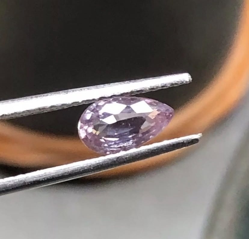 Pear-shaped lilac sapphire held in tweezers